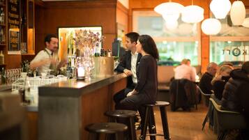 Un espace bar avec des tabourets, un comptoir et un barman. On aperçoit des tables et des chaises au fond.
