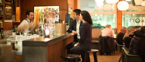A bar area with stools, a counter, and a bartender. There are tables and chairs in the background.