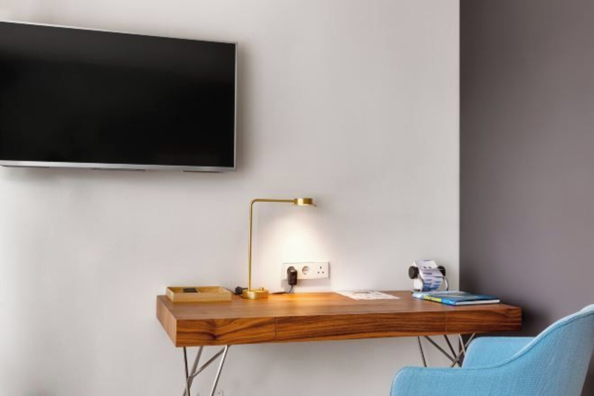 A modern room with a wooden desk, a mounted television, a desk lamp, and a chair.