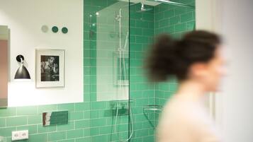 A bathroom with green tiles, a glass shower enclosure, a framed picture on the wall, and a towel rack.
