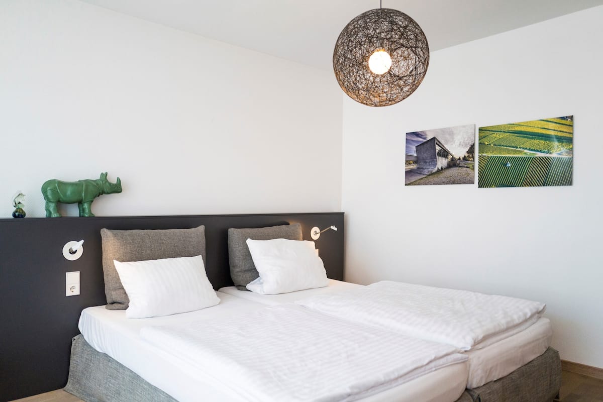 A bedroom with a bed, two pillows, a green animal decoration, a wall-mounted light fixture, and two framed pictures.