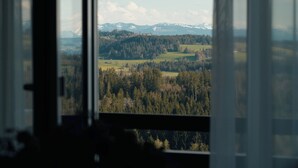 Une vue à travers une fenêtre sur un paysage composé d’arbres et de montagnes lointaines.