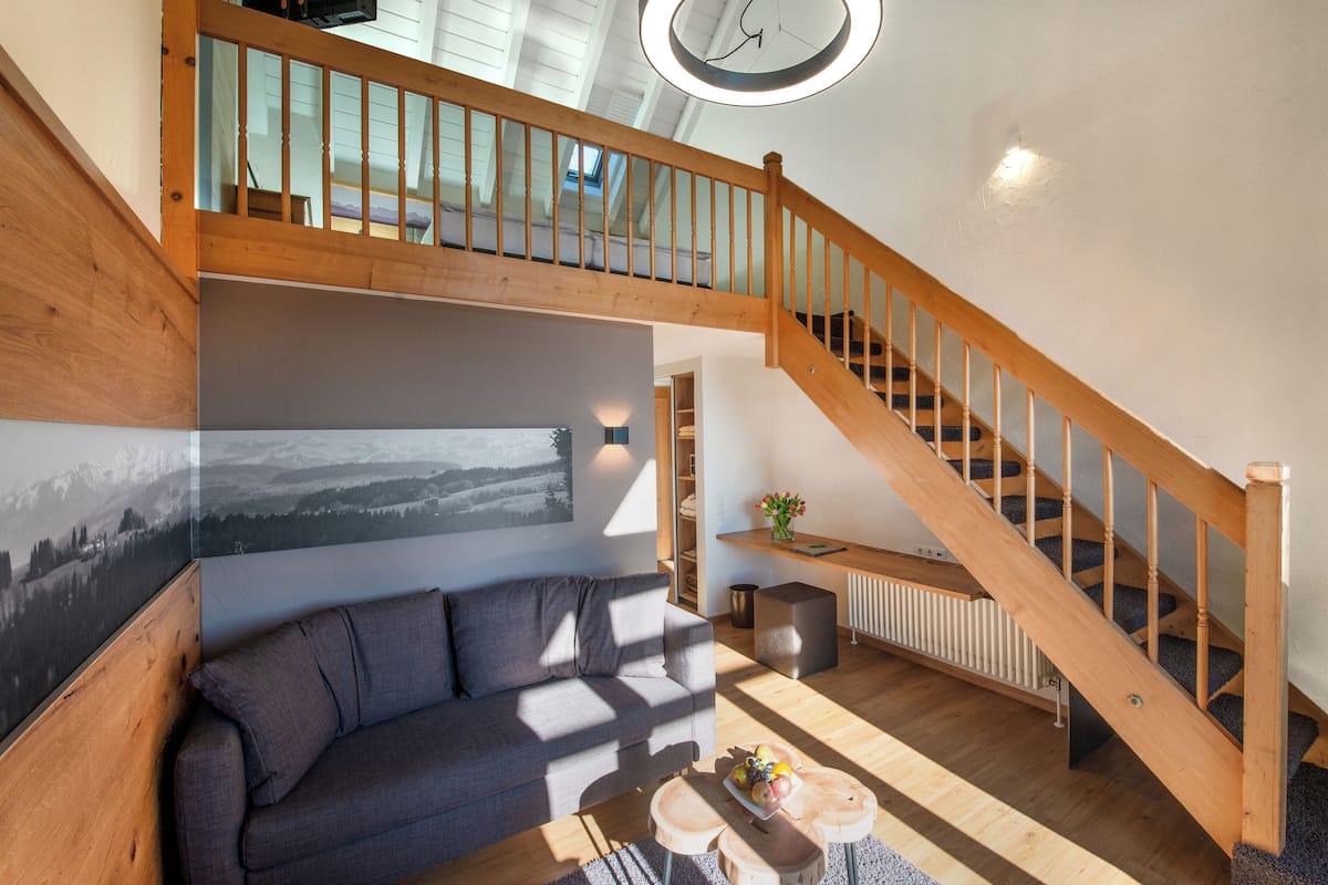 Un salon moderne avec un escalier en bois, un canapé, une table basse et une vue sur l’extérieur.