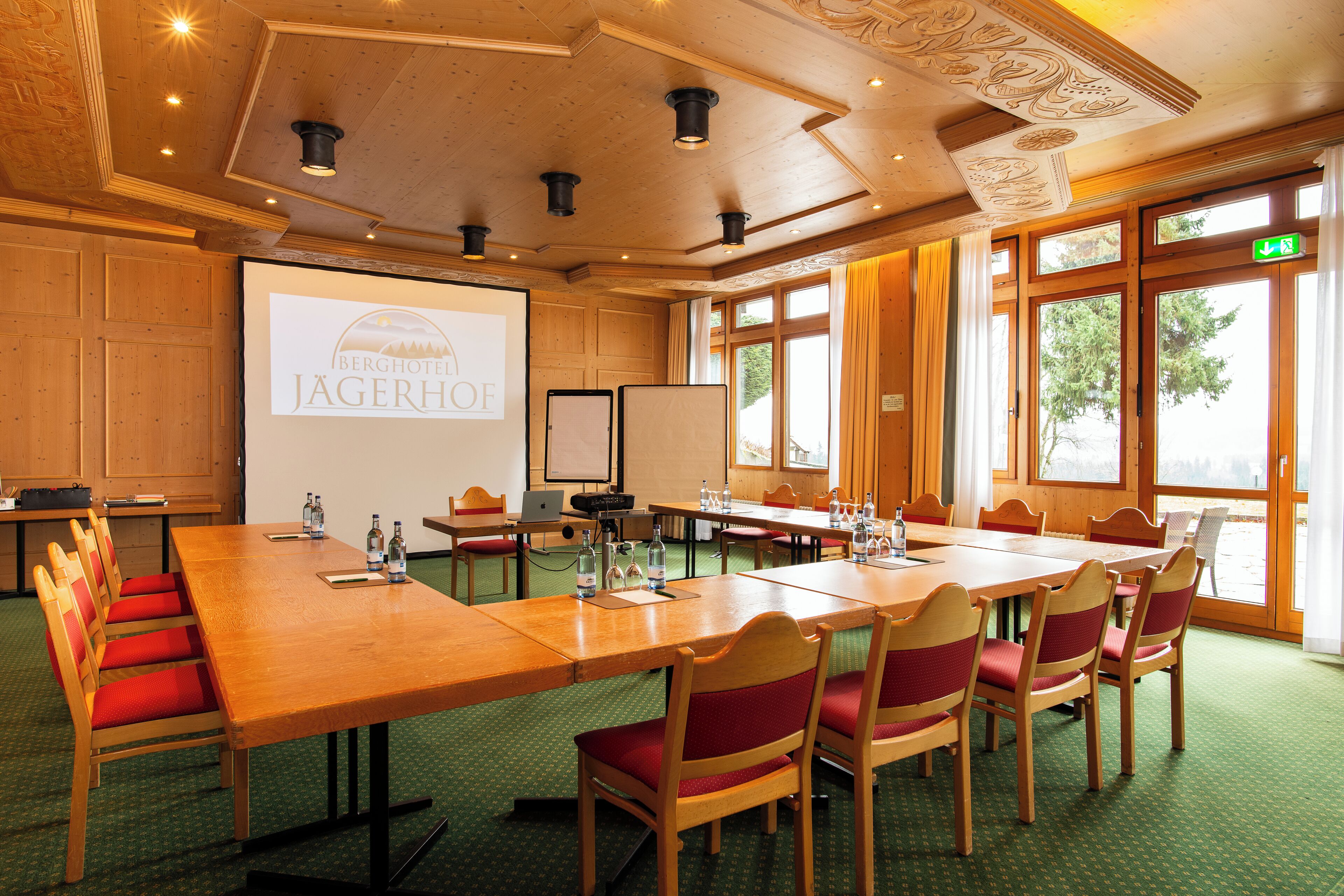 A conference room with a large table, chairs, a projector screen, and windows with curtains.