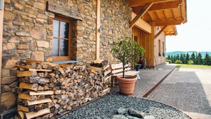 Un bâtiment en pierre avec une façade en bois, une fenêtre, une pile de bois de chauffage et un arbre en pot.