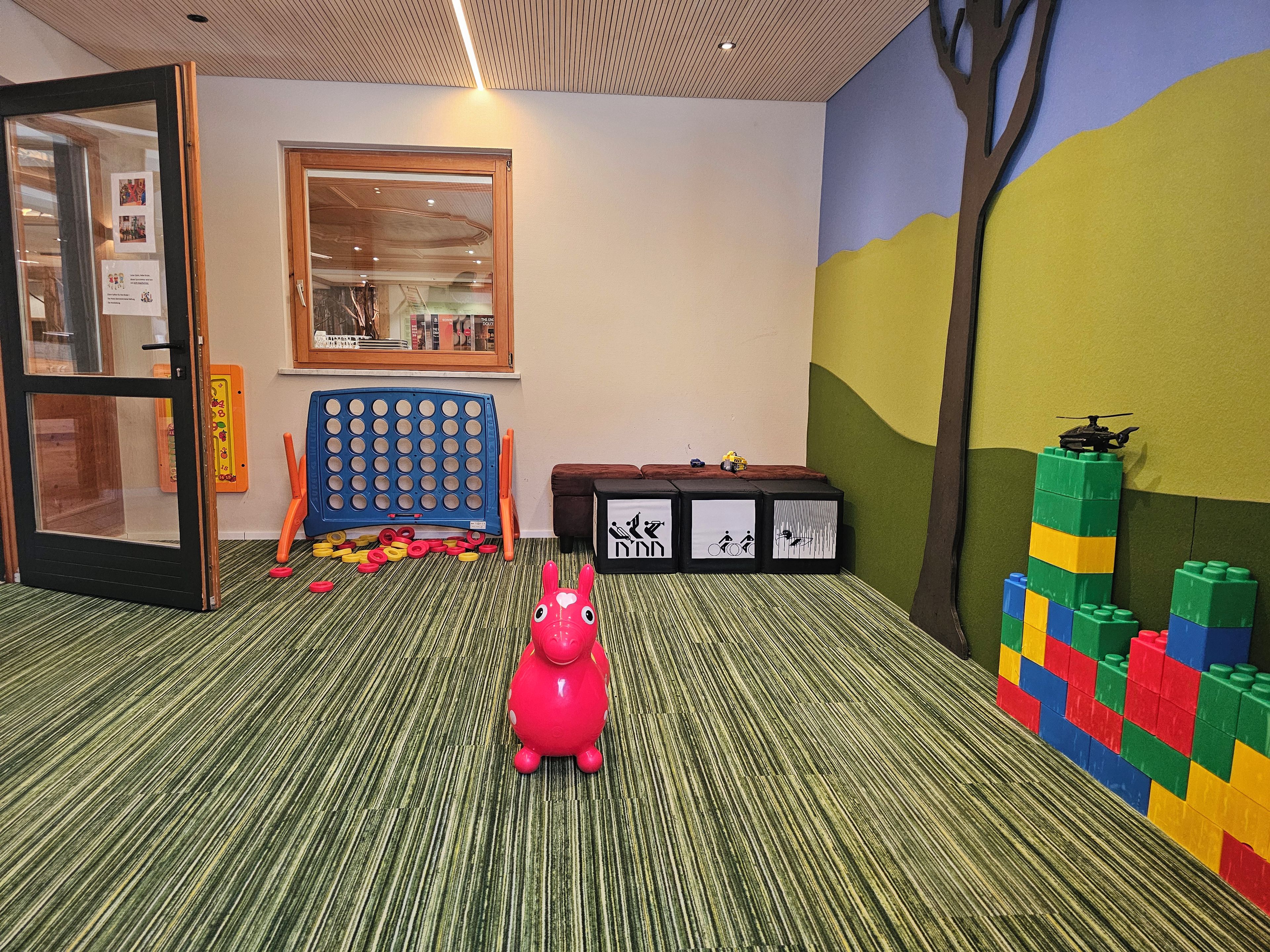 Ein Zimmer mit Teppichstreifen, einem rosafarbenen Spielzeug, einem blauen Spielbrett und bunten Bauklötzen.