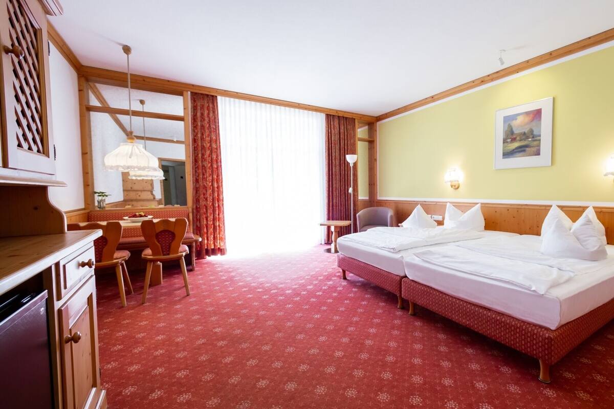 A hotel room with a bed, a desk, a chair, and a dining area.