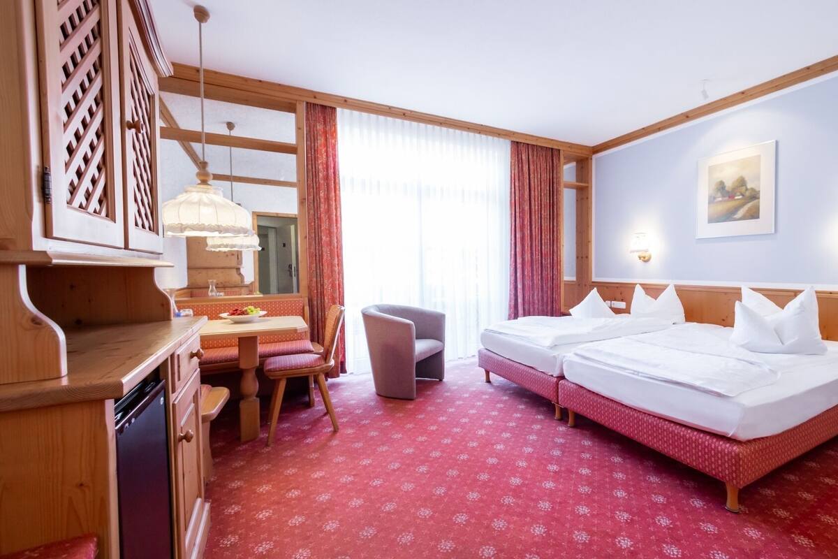 A hotel room with two beds, a desk, a chair, a dining table, and a red patterned carpet.