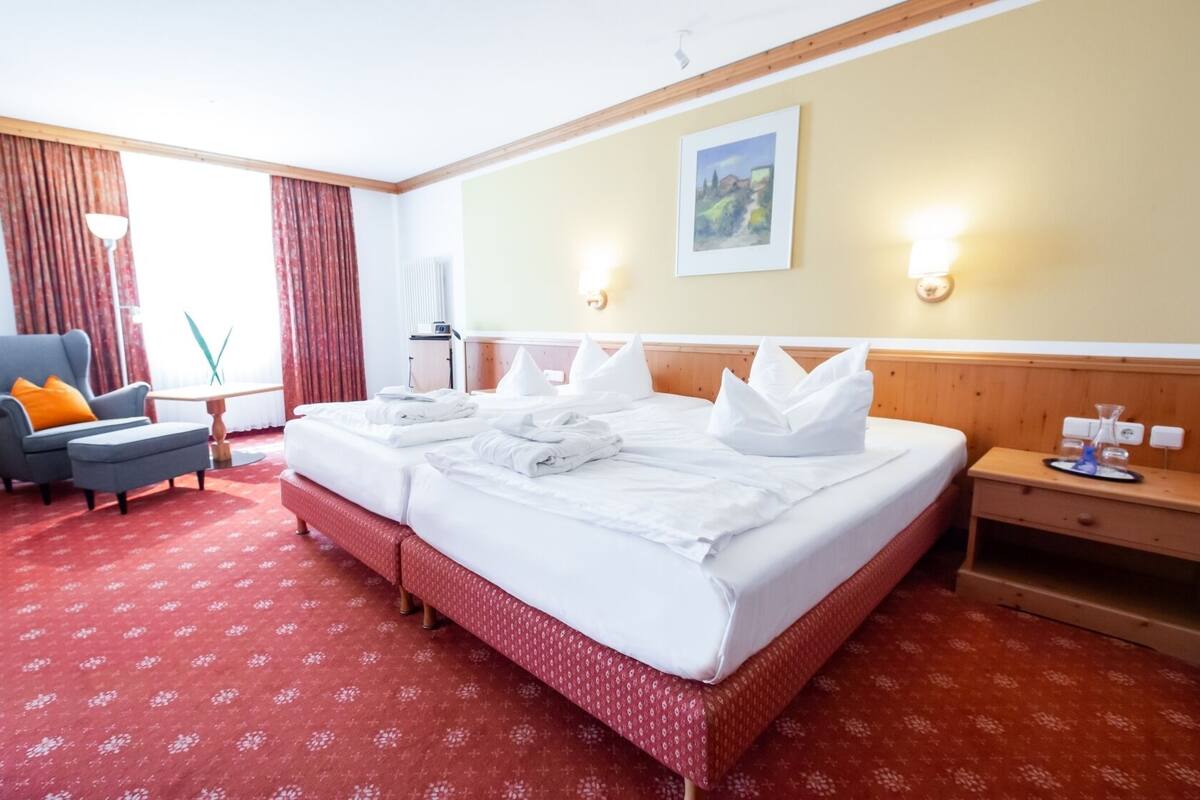 A hotel room with a large bed, a chair, a desk, and a painting on the wall.