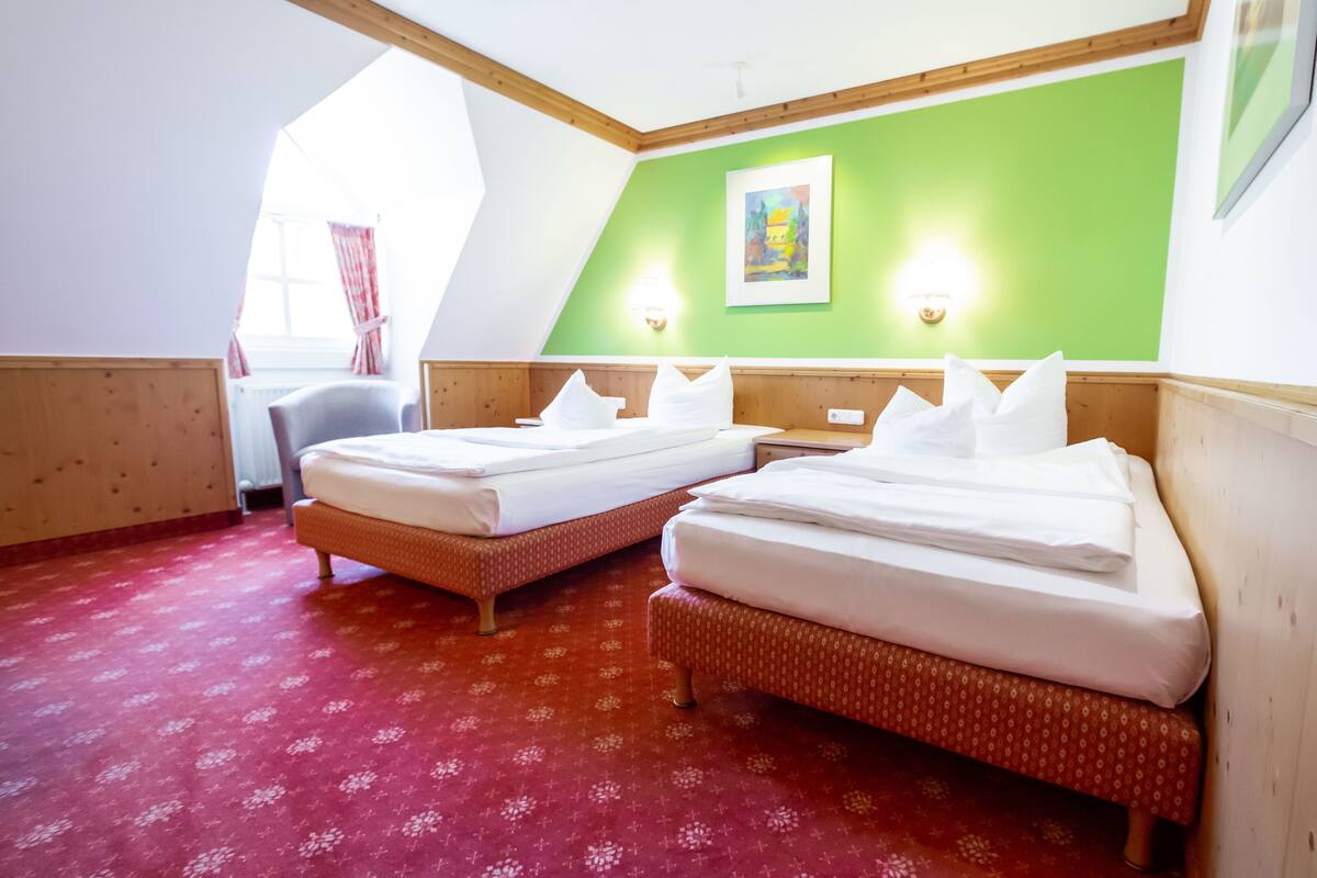 A hotel room with two beds, a green accent wall, and a window with curtains.