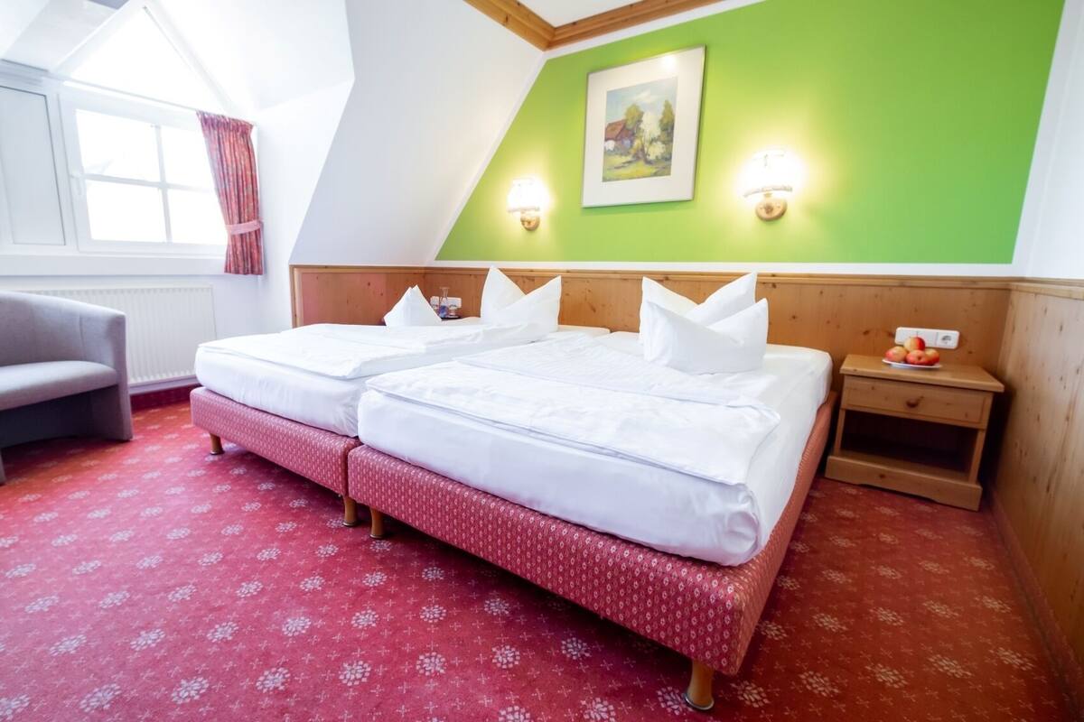 A room with two beds, a chair, and a small table with apples.
