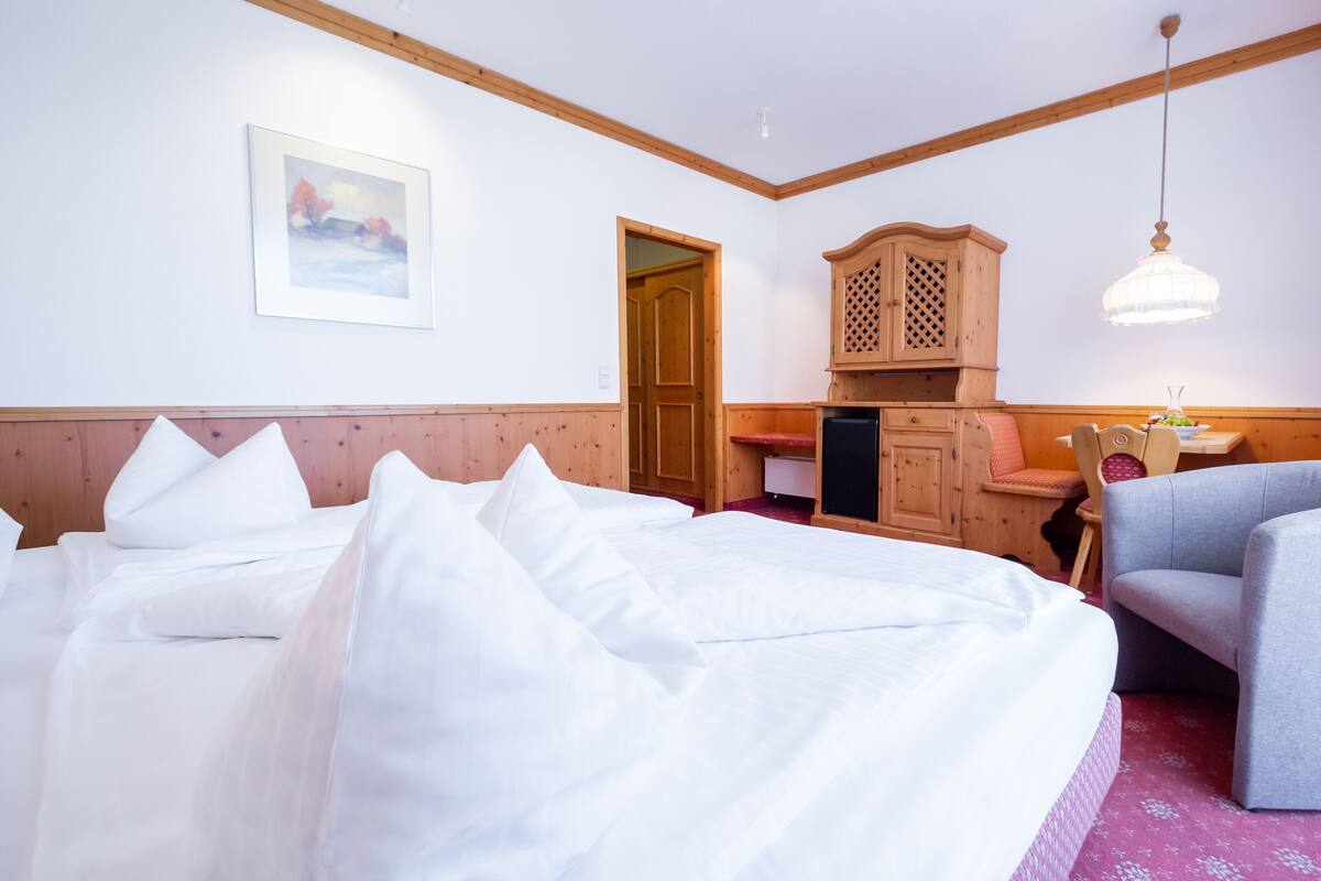 A hotel room with a bed, a chair, a small table, a refrigerator, and a wooden cabinet.
