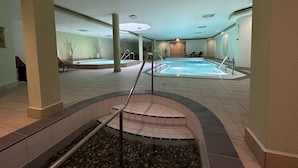 Una piscina interna con pavimento piastrellato, una piccola zona con scalini e sedie a sdraio.