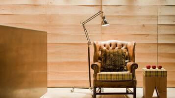 Une pièce aux murs lambrés, avec un fauteuil en cuir, une lampe de bureau et un petit tabouret en bois sur lequel sont posées des pommes.