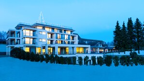 Un immeuble moderne à plusieurs étages, doté de balcons et de grandes fenêtres, entouré de neige et d’arbres.