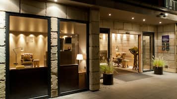A hotel entrance with stone walls, a reception desk, and seating areas visible through the glass doors.