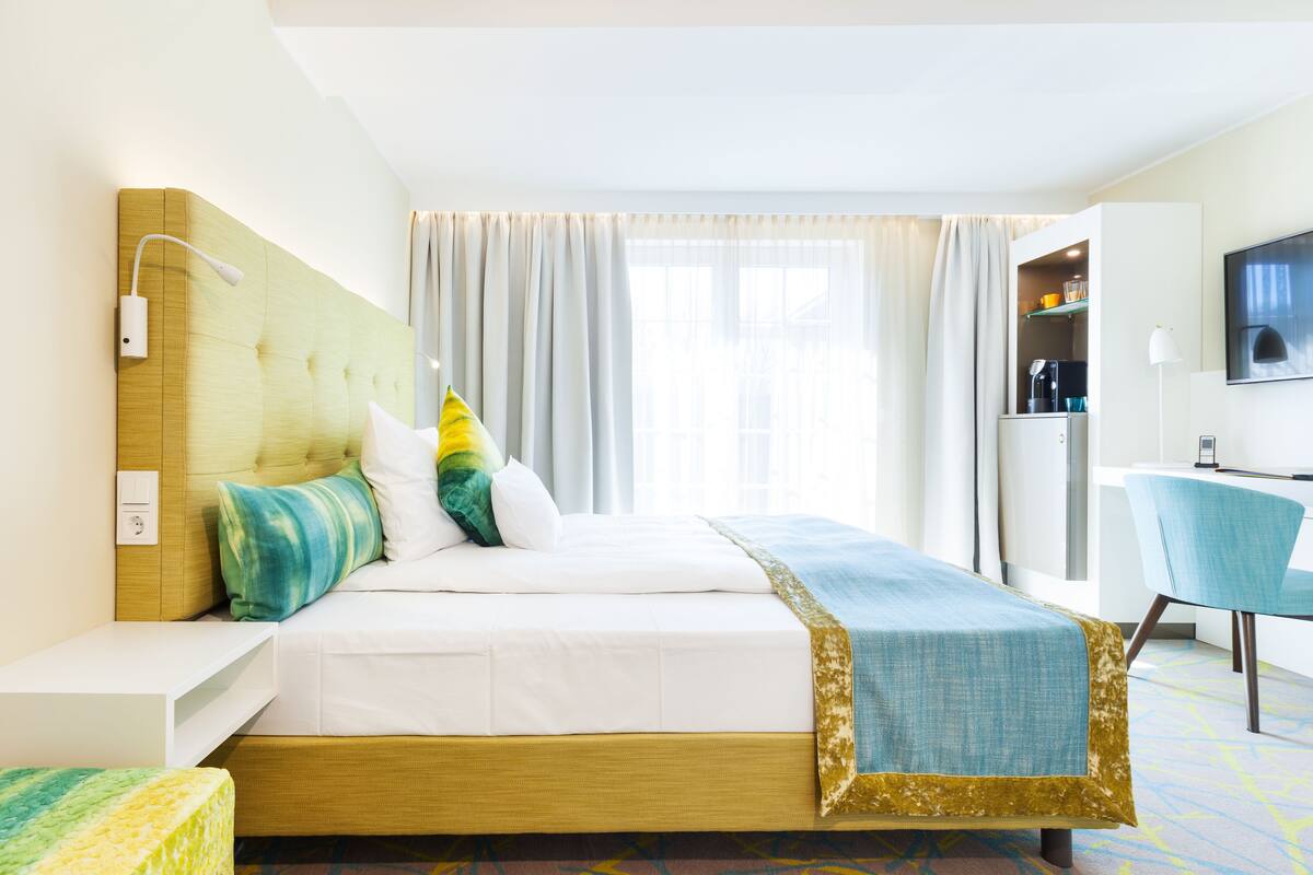A hotel room with a bed, a desk, a chair, a TV, and a window with curtains.