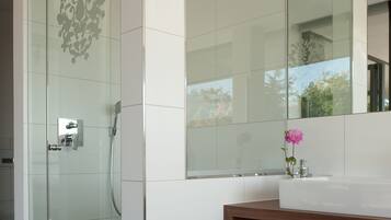 Un baño moderno con cabina de ducha de vidrio, un espejo grande y un tocador de madera con artículos de aseo.