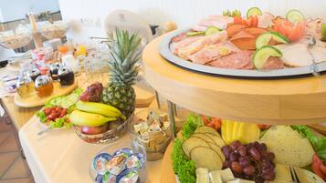 Une table de buffet proposant une variété d’aliments, notamment des fruits, des fromages et des viandes.