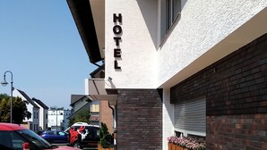 A hotel with a white facade, a visible 'HOTEL' sign, a brick wall with a window, and a paved driveway with bollards. - Garni-Hotel Bonnem-Inn (Bornheim)