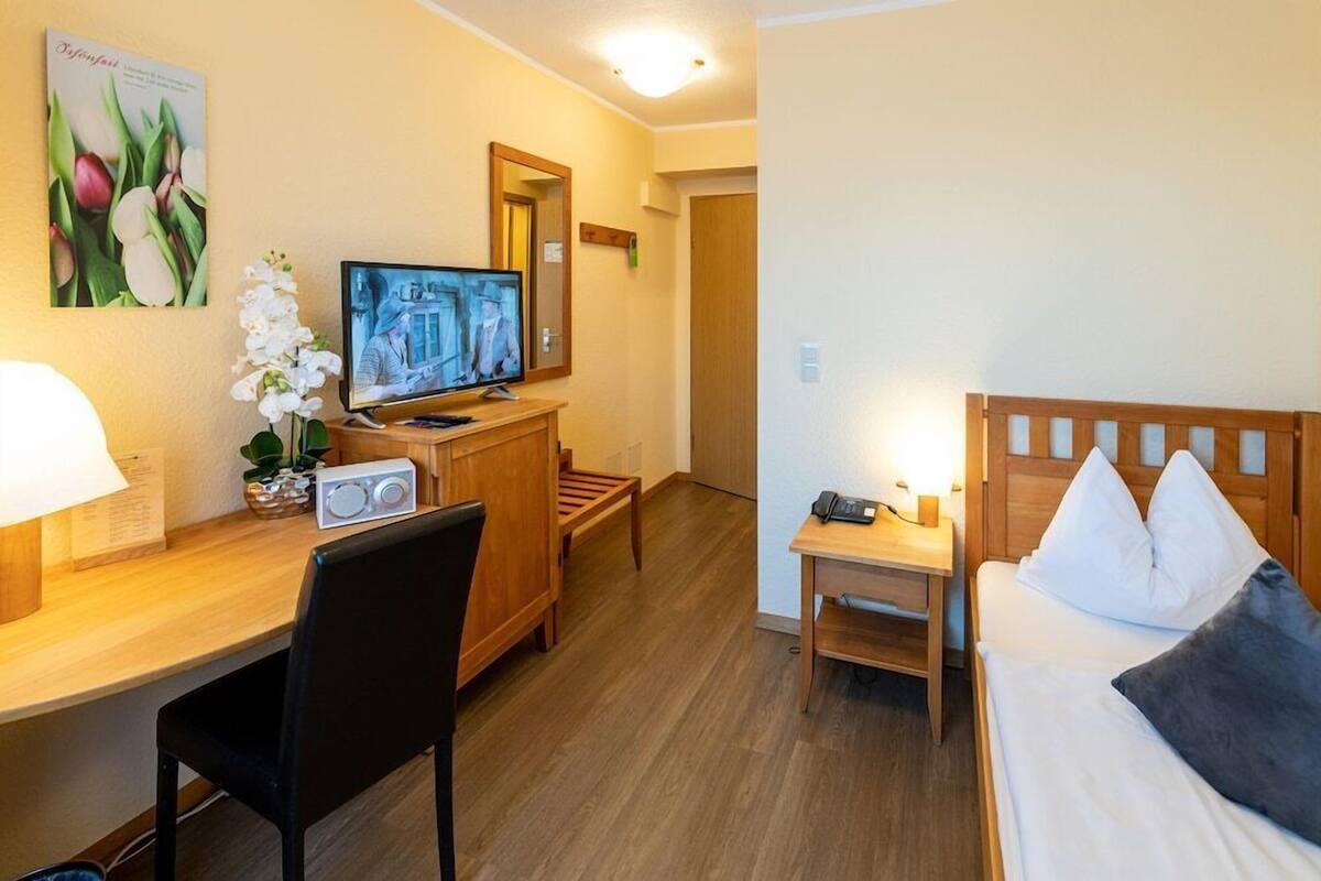 A hotel room with a bed, desk, chair, television, and a small table with a phone.