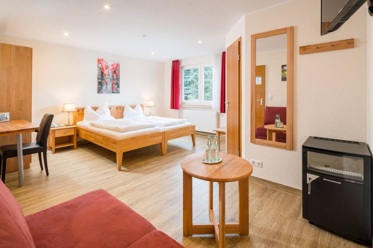 A hotel room with a bed, desk, chair, and a small table with bottles.