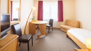 A hotel room with a bed, a desk with a chair, a television, a lamp, and a window with curtains. - Garni-Hotel Bonnem-Inn (Bornheim)