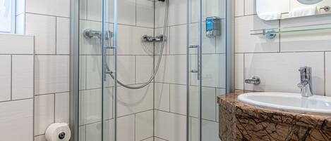 A modern bathroom with a glass-enclosed shower, a sink with a marble countertop, and a mirror above the sink.