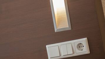 Een hotelkamer met een houten hoofdeinde, een telefoon op het nachtkastje en een wandlamp.