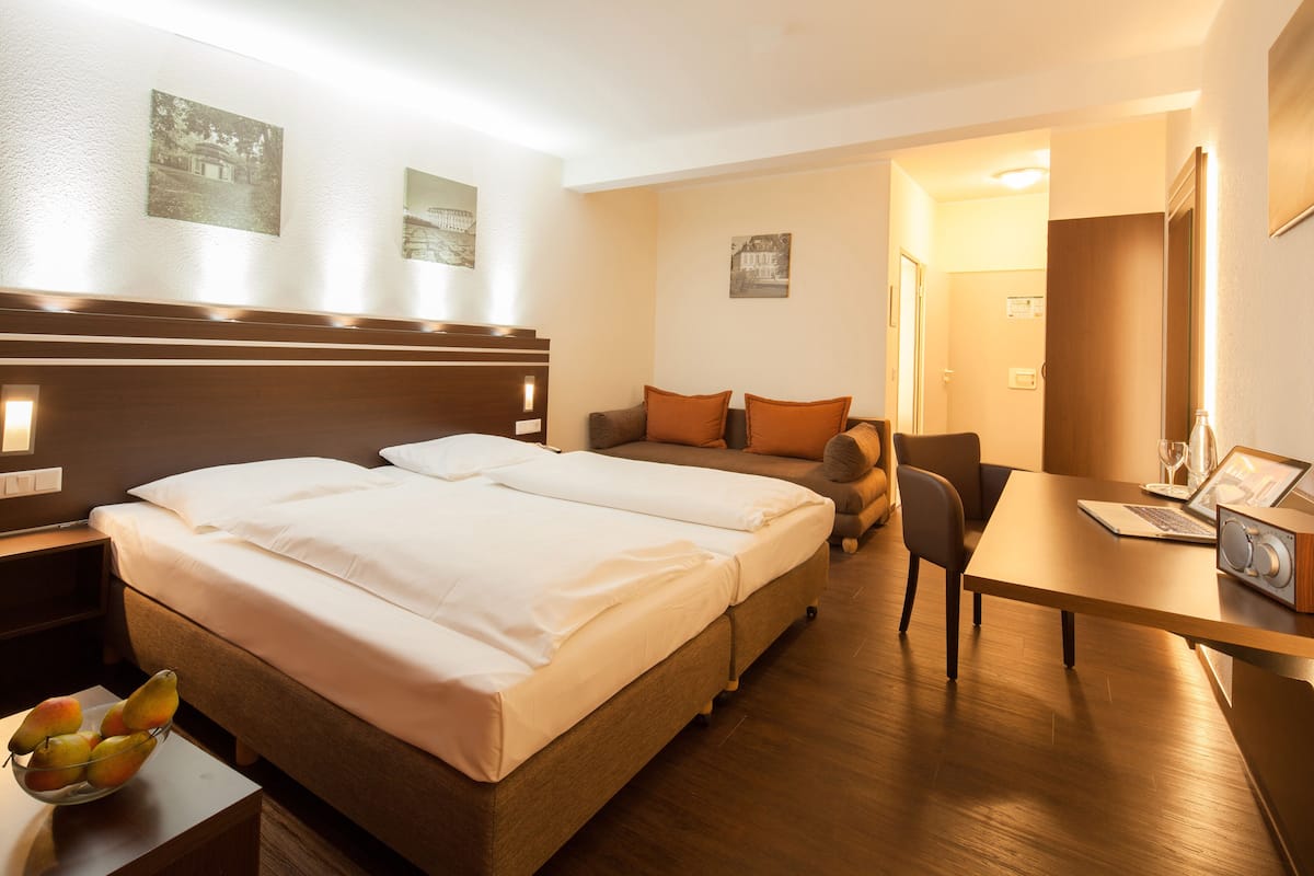 Une chambre d’hôtel avec un lit double, un bureau avec un ordinateur portable, une chaise et une petite table sur laquelle se trouve un panier de fruits.