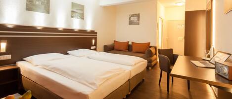 Une chambre d’hôtel avec un lit double, un bureau avec un ordinateur portable, une chaise et une petite table sur laquelle se trouve un panier de fruits.