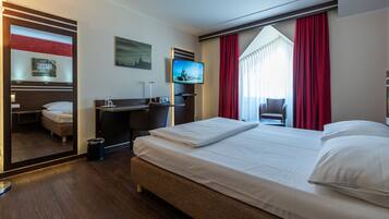 A hotel room with a large bed, a desk, a TV, and a window with red curtains.