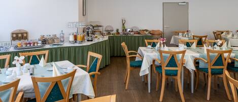 Een eetruimte met meerdere tafels en stoelen, een buffetopstelling en een verscheidenheid aan eten en drinken.