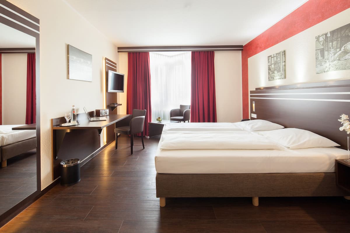 Une chambre d’hôtel avec un lit, un bureau et une chaise, une télévision et une fenêtre avec des rideaux.