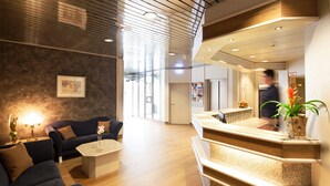 Un vestíbulo moderno con mostrador de recepción, escalera y zona de estar con mesa de centro y sofás.