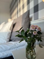A bed with white bedding and a vase with flowers on a bedside table.
