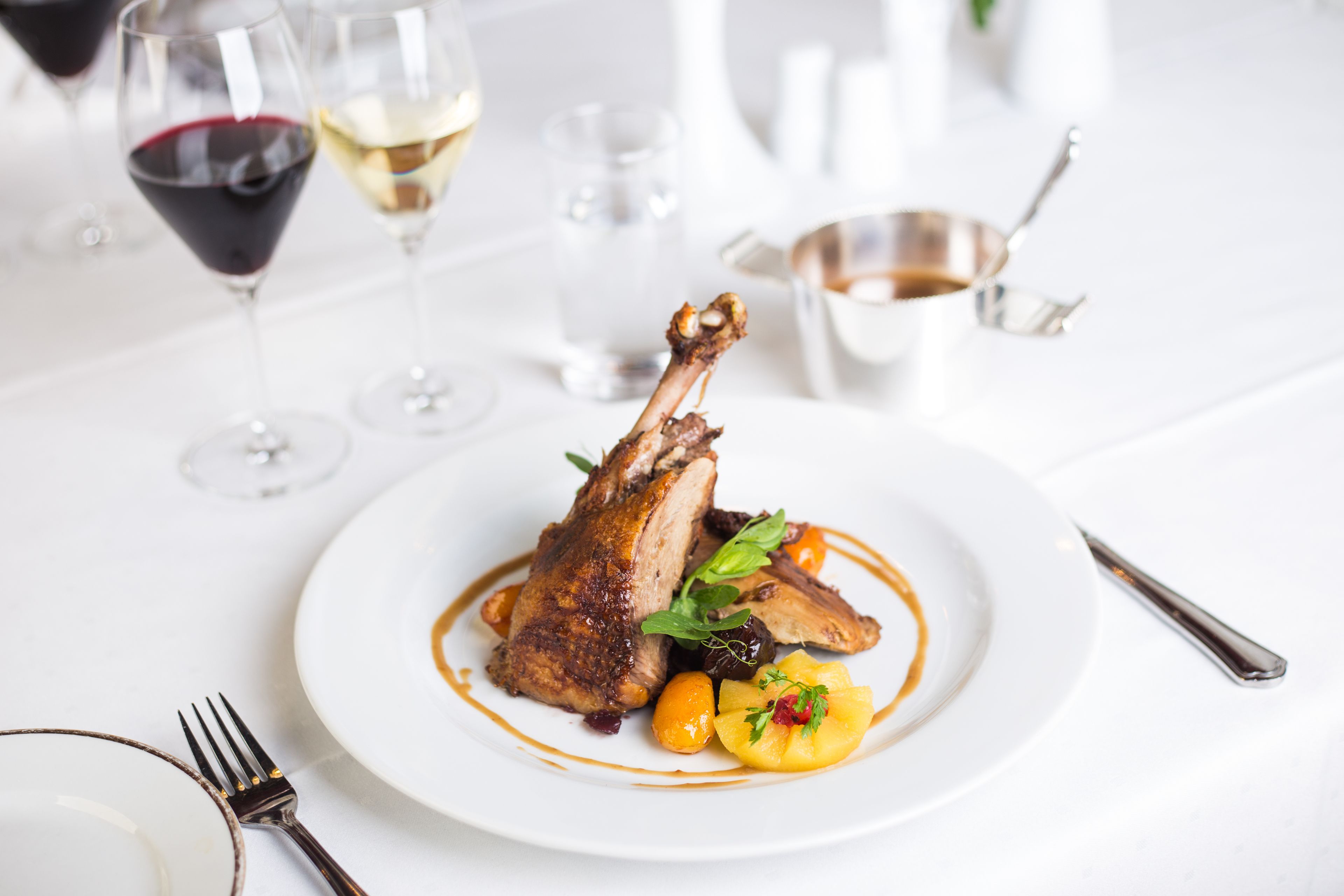 Une table de salle à manger blanche, avec une assiette de nourriture, une fourchette et un verre de vin rouge.