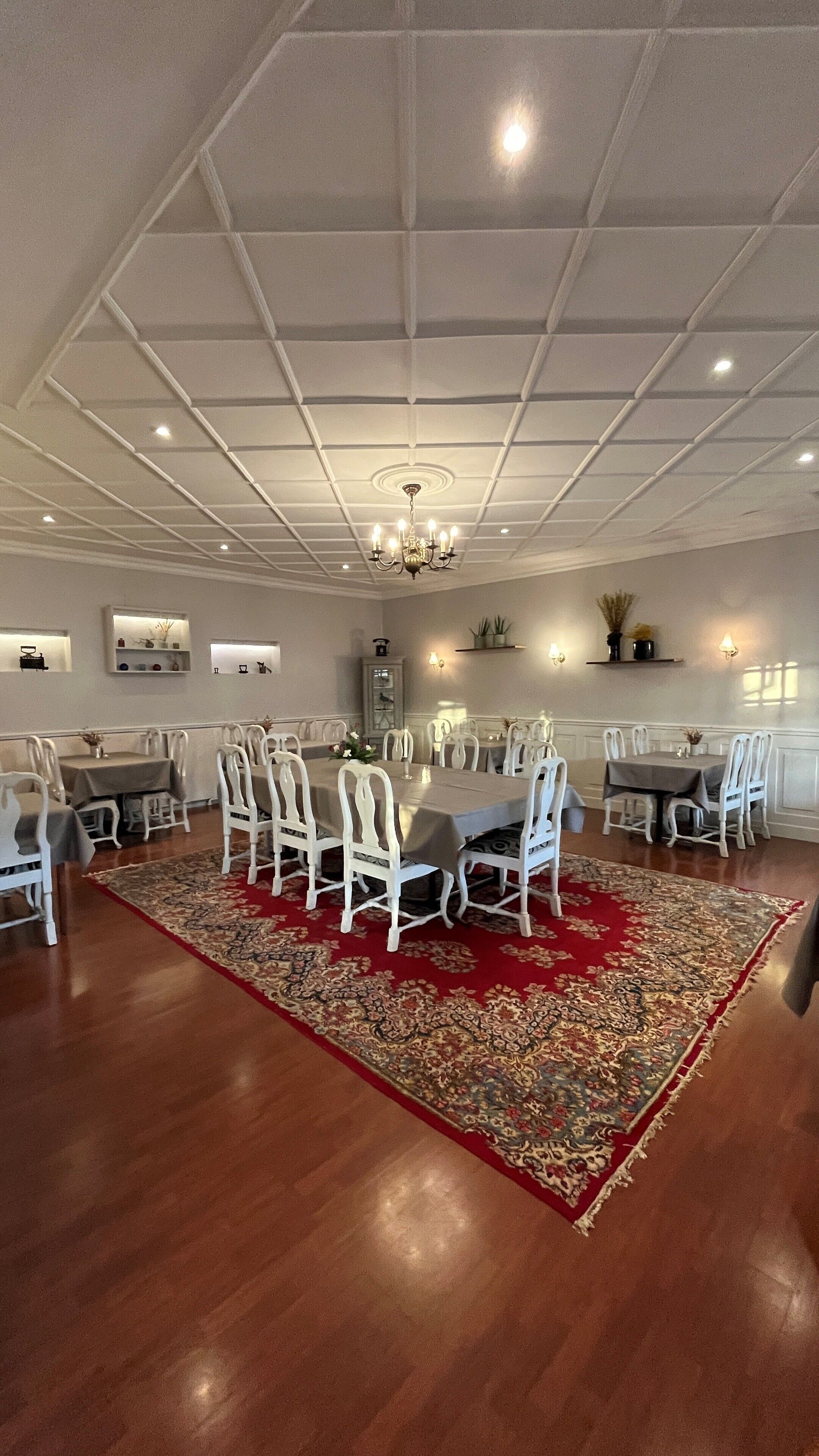 A spacious dining area with a large table and chairs, a chandelier, and a patterned rug.