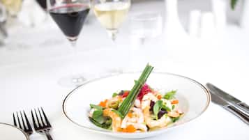 A plate of shrimp salad with a garnish, accompanied by wine glasses and cutlery on a white table.