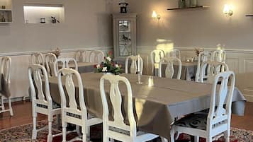 A dining room with a large table, white chairs, a chandelier, and a red carpet.