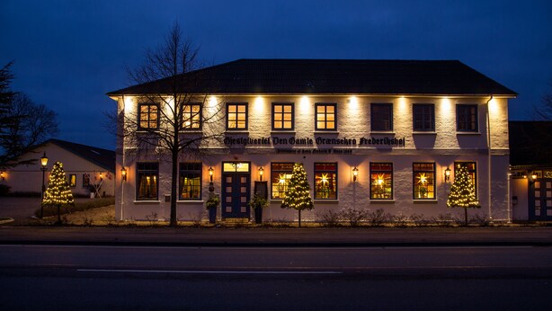 A building with multiple lit windows and a Christmas tree in front. - Den Gamle Grænsekro (Christiansfeld)