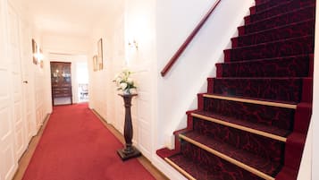 A hallway with a red carpet leading to a staircase with red carpeted steps and a wooden handrail.