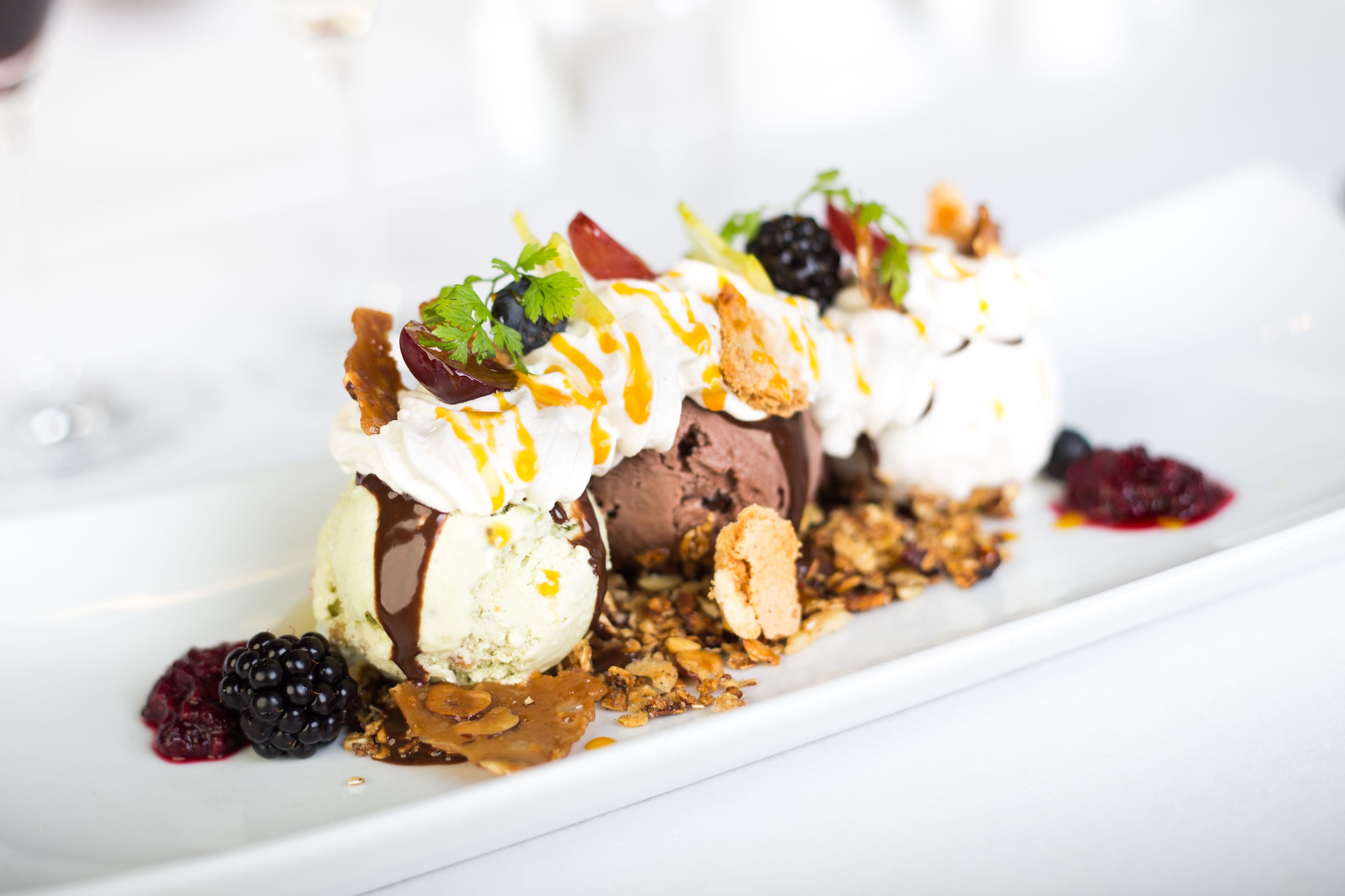A dessert with ice cream, berries, and nuts on a white plate.