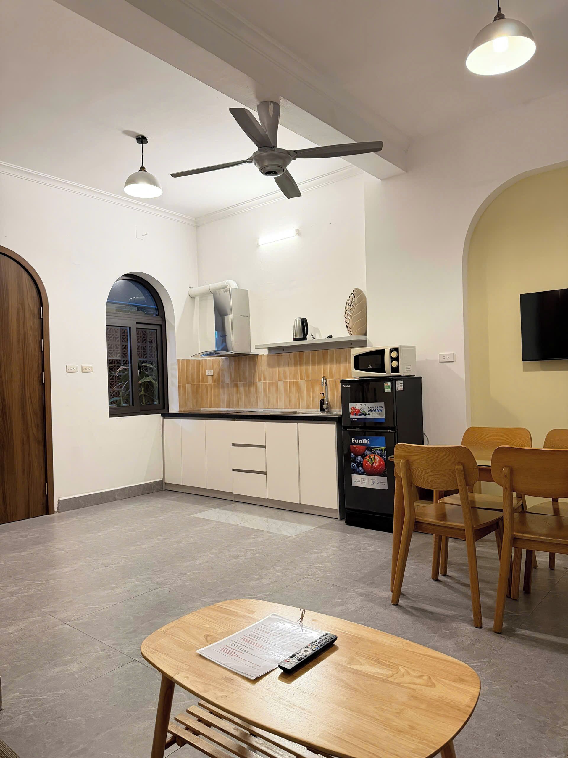 A modern kitchen with a microwave, refrigerator, and wooden cabinets. There is a dining area with a table and chairs.