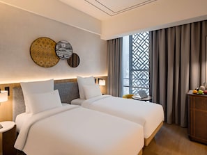 Habitación de hotel con dos camas, una mesa pequeña con una laptop, una mesita de mimbre y una ventana con cortinas.