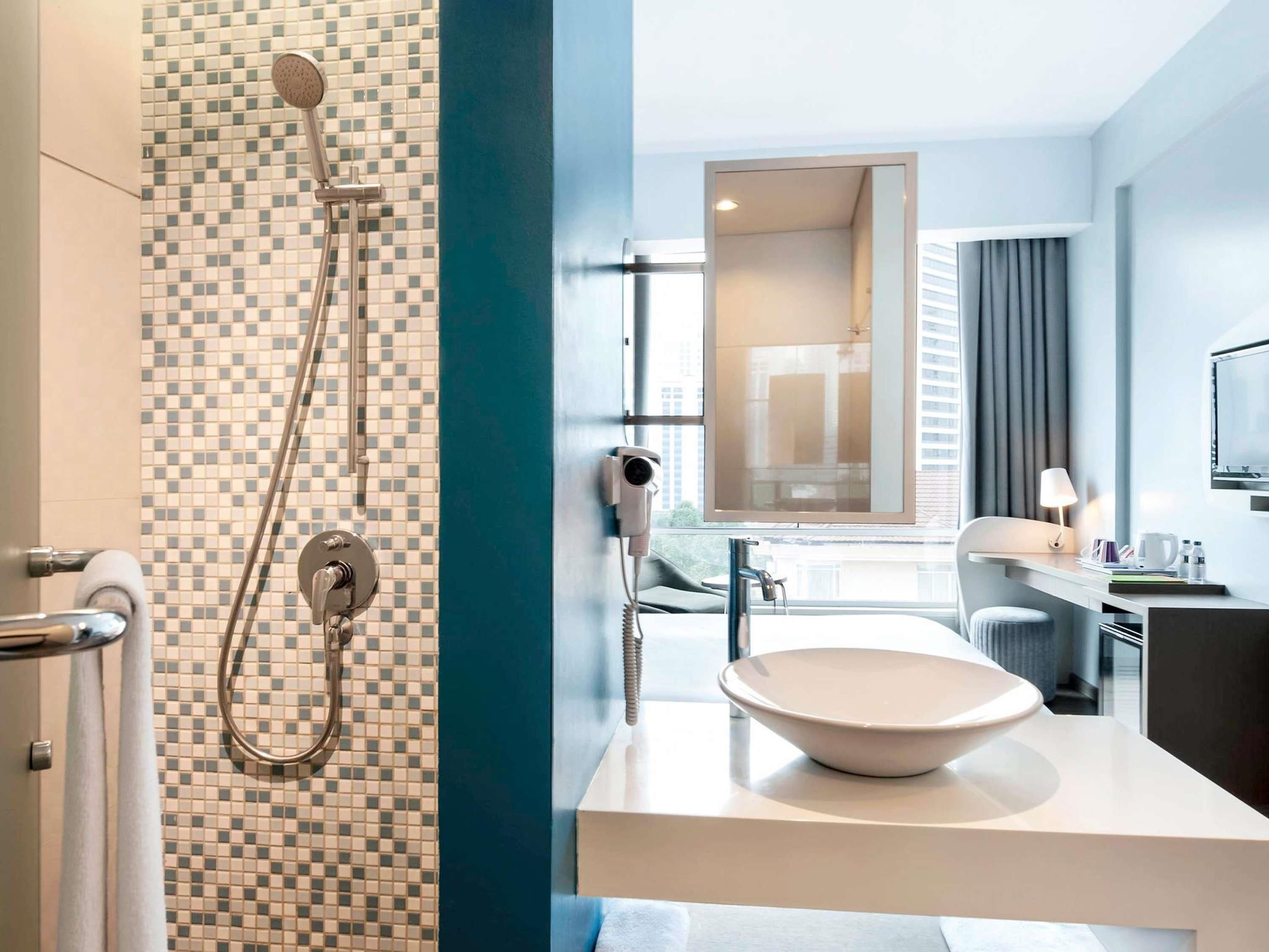 Une salle de bain moderne équipée d’une douche, d’un lavabo avec un grand bac, d’un porte-serviettes et d’un miroir.