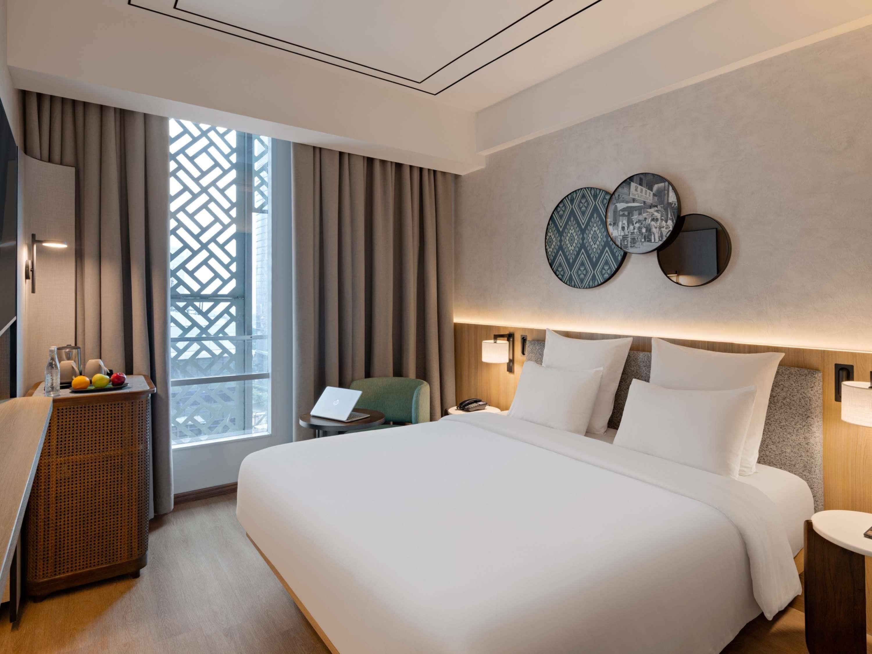A hotel room with a large bed, a desk with a laptop, a chair, and a window with curtains.