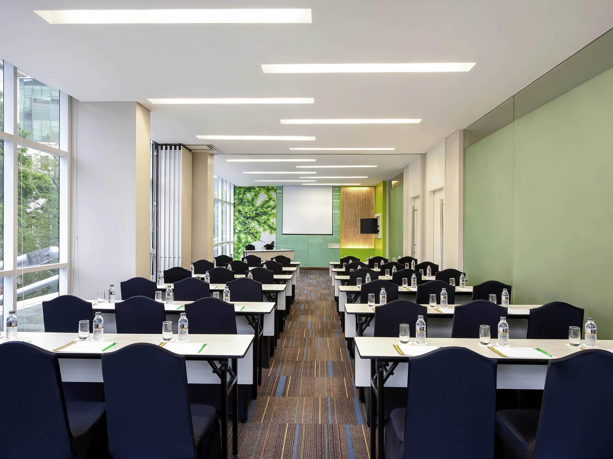 A conference room with rows of tables, chairs, and a projector screen.