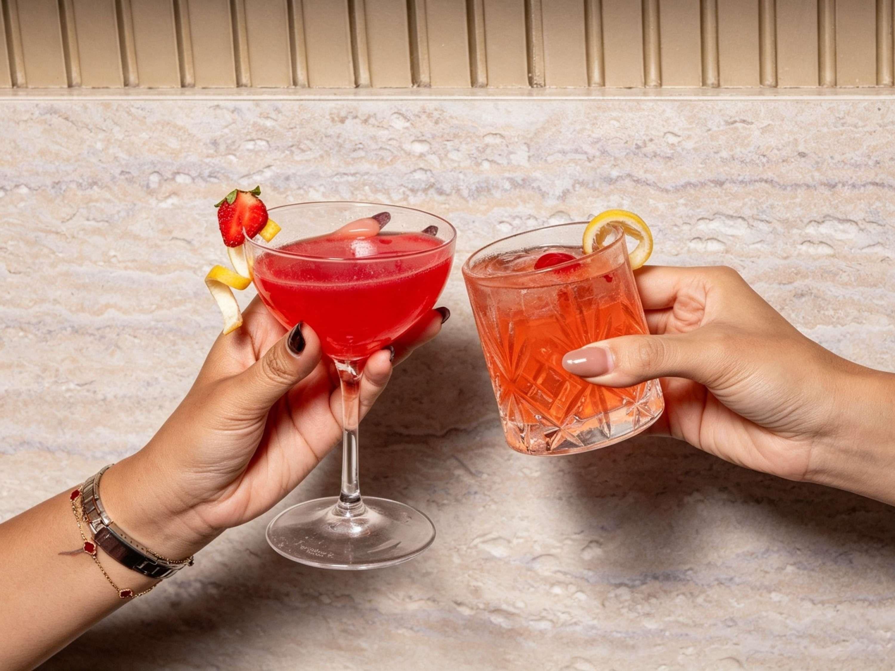 Två händer håller i cocktailglas dekorerade med frukt.