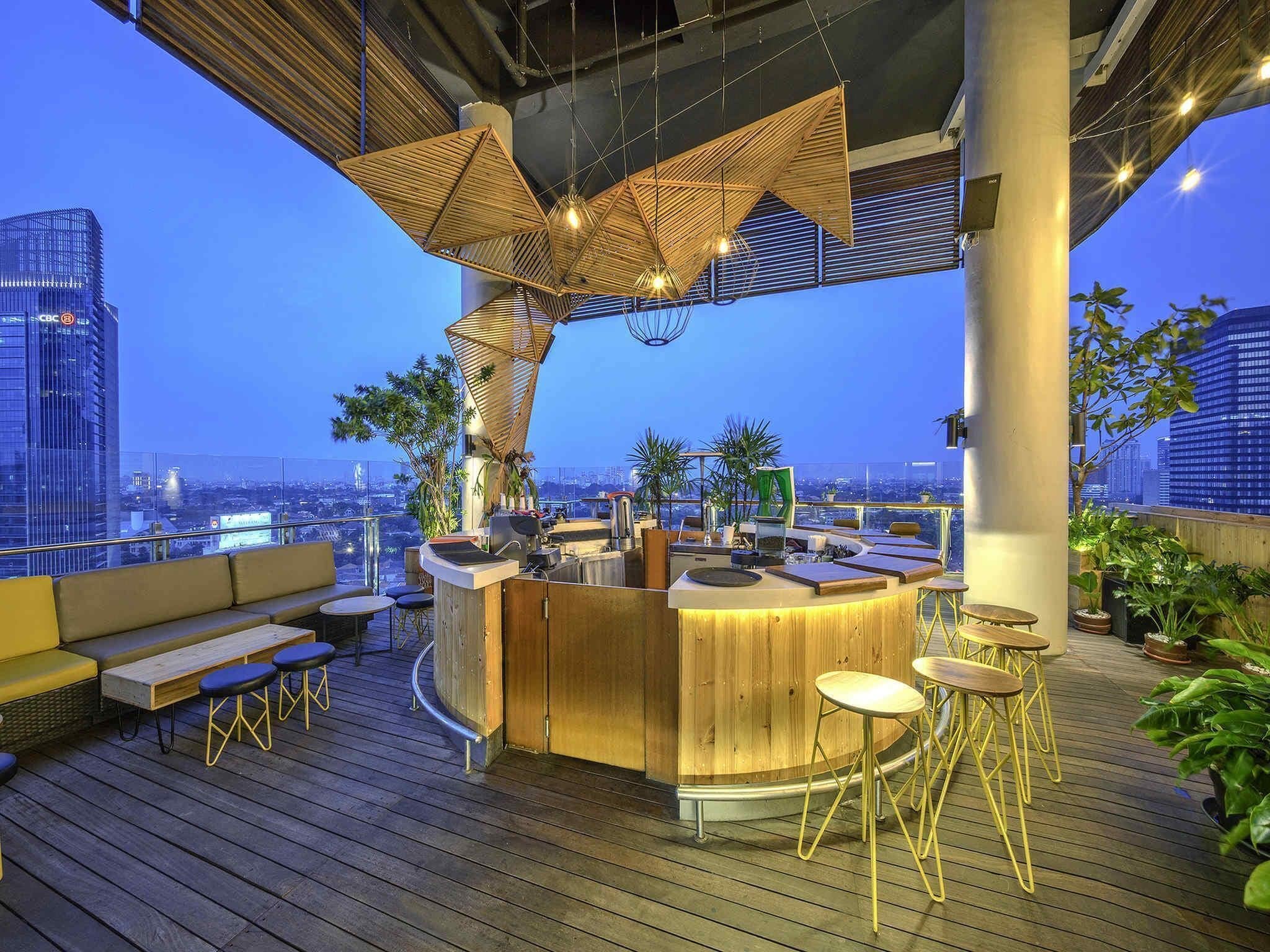 A rooftop bar with a wooden bar counter, seating, and potted plants.